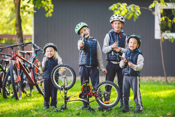 Παιδομηχανική, επισκευή ποδηλάτου. Ευτυχισμένα παιδιά που φτιάχνουν ποδήλατο έξω στην ηλιόλουστη μέρα. Σχέδιο επισκευής ποδηλάτων. Ομαδική εργασία οικογένεια ποζάρουν με εργαλεία για την επισκευή ενός ποδηλάτου στα χέρια έξω — Φωτογραφία Αρχείου