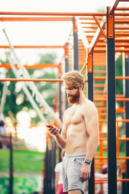 Atletik görünümlü akıllı telefon. Akıllı saatle bilekte. Sporcu antrenmandan sonra performansları kontrol ediyor. Fitness, spor, yaşam tarzı konsepti. Adam fitness uygulaması kullanıyor. Beden eğitiminde portre adam dinlenme egzersizi yapıyor.