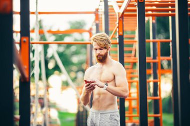 Atletik görünümlü akıllı telefon. Akıllı saatle bilekte. Sporcu antrenmandan sonra performansları kontrol ediyor. Fitness, spor, yaşam tarzı konsepti. Adam fitness uygulaması kullanıyor. Beden eğitiminde portre adam dinlenme egzersizi yapıyor.