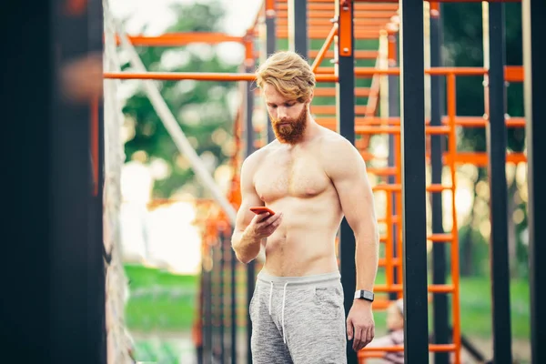 Athlete looking smart phone. On wrist with smart watch. Sportsman checking performances after training. Fitness, sport, lifestyle concept. man using fitness app. Portrait guy in gym resting workout — Stock Photo, Image