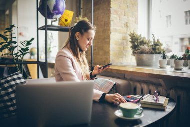 Kahve masasında oturan, kahve içen ve akıllı telefon kullanan bir kadın. Kafede Telefon Kullanan Kadın. Öğrenci çevrimiçi öğreniyor. Kız mailleri kontrol ediyor. Kadın Kafe, cep telefonu kullan, çalışan defter