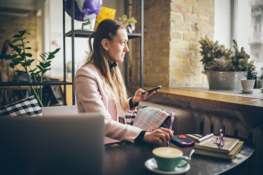 Kahve masasında oturan, kahve içen ve akıllı telefon kullanan bir kadın. Kafede Telefon Kullanan Kadın. Öğrenci çevrimiçi öğreniyor. Kız mailleri kontrol ediyor. Kadın Kafe, cep telefonu kullan, çalışan defter