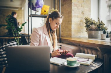 Kahve masasında oturan, kahve içen ve akıllı telefon kullanan bir kadın. Kafede Telefon Kullanan Kadın. Öğrenci çevrimiçi öğreniyor. Kız mailleri kontrol ediyor. Kadın Kafe, cep telefonu kullan, çalışan defter
