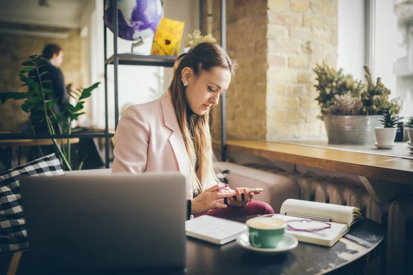 Mujer sentada cafetería mesa de madera, beber café y el uso de teléfono inteligente. Mujer usando el teléfono en el café. Aprendizaje de estudiantes online. Chica revisando correo electrónico. Mujer Café, uso de teléfono móvil, Cuaderno de trabajo — Foto de Stock