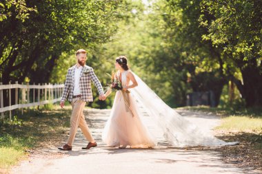 Güzel bir düğün çifti ormanı. Gelin ve damat, beni takip edin, evli çift, beyaz gelinlik ve duvak giyen kadın. Kırsal kesim aşk hikayesi. Hipster fotoğrafımı takip et. Yeni evliler el ele yürüyorlar.