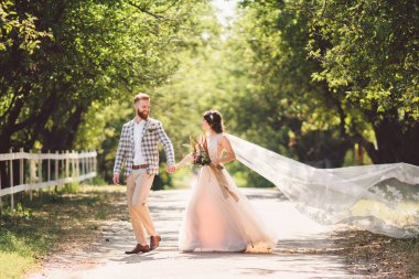 Güzel bir düğün çifti ormanı. Gelin ve damat, beni takip edin, evli çift, beyaz gelinlik ve duvak giyen kadın. Kırsal kesim aşk hikayesi. Hipster fotoğrafımı takip et. Yeni evliler el ele yürüyorlar.