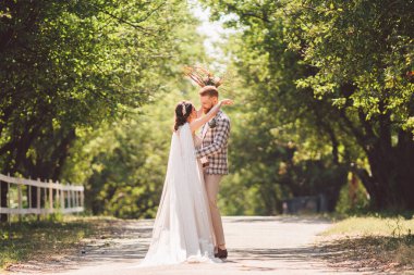 Damat mutlu gelini kucaklıyor. Gün batımı güneşli hava. Mutlu yeni evliler bahçede yan yana duruyor. temalı bir düğün portresi ve güzel bir gelinlik. Düğün çifti dışarıda sarılıp öpüşüyor.