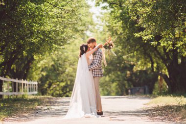 Damat mutlu gelini kucaklıyor. Gün batımı güneşli hava. Mutlu yeni evliler bahçede yan yana duruyor. temalı bir düğün portresi ve güzel bir gelinlik. Düğün çifti dışarıda sarılıp öpüşüyor.