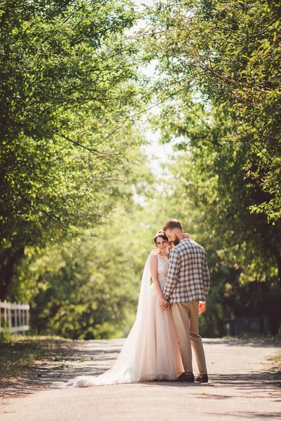 新郎は陽気な花嫁の夕日晴れた日を包含します。庭には新婚夫婦が一緒に立っている。テーマウェディングポートレートと美しいウェディングホワイトドレス。結婚式のカップル抱擁とキス屋外 — ストック写真