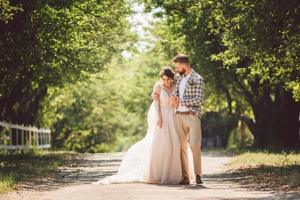 Wedding couple enjoys walking in the woods. Newlyweds hug and hold hands. Newlyweds walk forward holding hand in the park along the path in sunny weather. Wedding and engagement theme — Stock Photo, Image