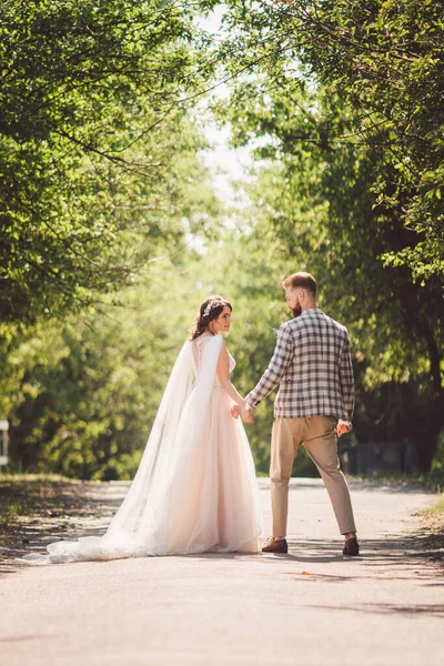 Noivo abraça alegre noiva pôr-do-sol tempo ensolarado. Felizes recém-casados juntos no jardim. retrato de casamento tema e vestido branco de casamento bonito. casamento casal abraço e beijo ao ar livre — Fotografia de Stock