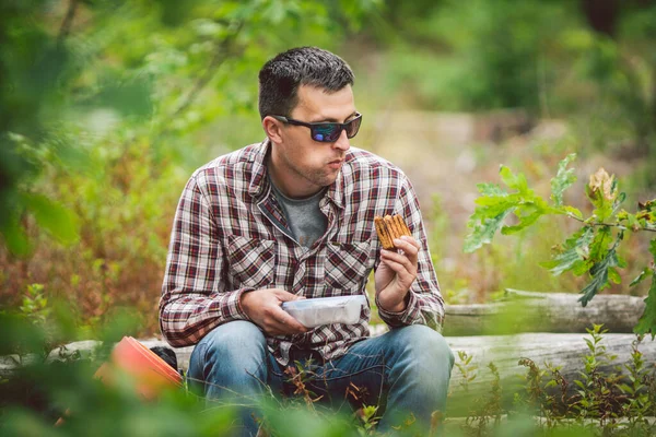 Hungry man eating. Sandwich outdoors. hiker eating sandwich sitting in forest. tourist eat snack food. Hiker take break with time for food. Caucasian guy tourist bring splastic box with sandwich