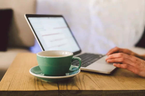 Primeros planos de la mujer de negocios manos utilizando el ordenador portátil con café taza. Manos de mujer Teclado de computadora en la cafetería. smartphone y taza caliente Cappuccino en la mesa. Concepto de estilo de vida de la gente. Tema independiente — Foto de Stock