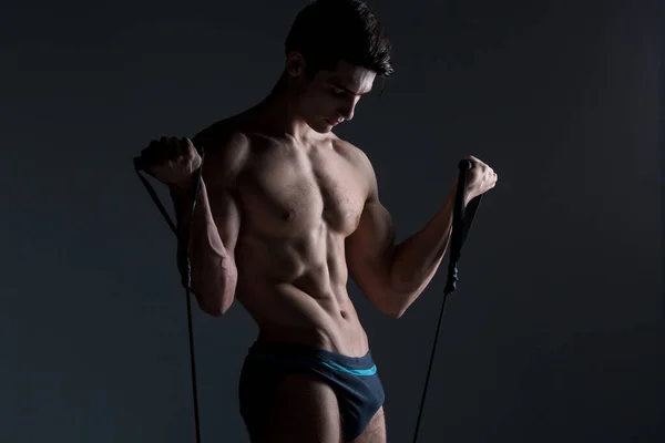 Kas Fitness genç erkek antika mükemmel kaslar altı paketleri ABS ve çıplak göğüs. Stüdyodan karanlık bir arka plana karşı streç elastik ile vücut geliştirmeci Model trenler. Egzersiz eğitim spor salonu — Stok fotoğraf