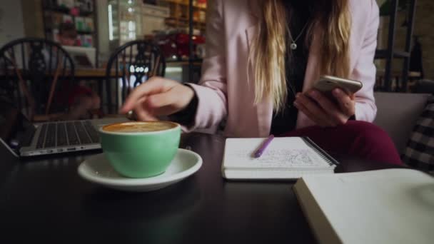 Γυναίκα κάθεται καφετέρια ξύλινο τραπέζι, πίνοντας καφέ και χρησιμοποιώντας smartphone. Γυναίκα που χρησιμοποιεί το τηλέφωνο στο καφέ. Μαθητής μαθαίνει online. Κορίτσι ελέγχει e-mail. Woman Cafe, χρήση κινητού τηλεφώνου, Working Notebook — Αρχείο Βίντεο