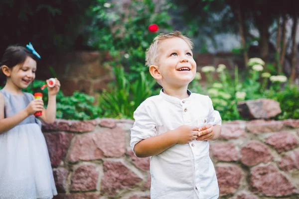 Zwei Kinder im Park pusten Seifenblasen und haben Spaß. Zwei Babys spielen mit Seifenblasen. Bruder und Schwester Spaß an der frischen Luft, glückliche Kindheit — Stockfoto