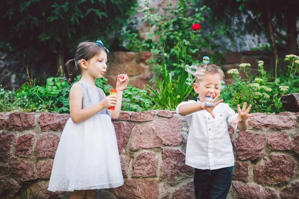 Zwei Kinder im Park pusten Seifenblasen und haben Spaß. Zwei Babys spielen mit Seifenblasen. Bruder und Schwester Spaß an der frischen Luft, glückliche Kindheit — Stockfoto