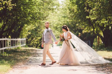 Güzel bir düğün çifti ormanı. Gelin ve damat, beni takip edin, evli çift, beyaz gelinlik ve duvak giyen kadın. Kırsal kesim aşk hikayesi. Hipster fotoğrafımı takip et. Yeni evliler el ele yürüyorlar.