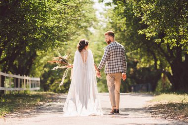 Mutlu gelin ve damat el ele tutuşup bahçede yürüyorlar. Park Ormanı 'nda yürürken el ele tutuşan çekici, yeni evlilerin arka planı. Gelecekteki yaşama giden yol. Mutlu evlilik anları