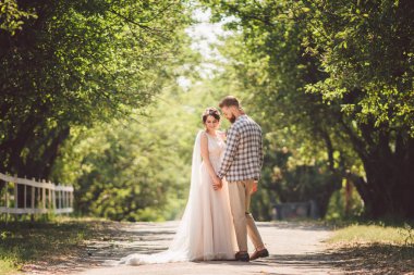 Damat mutlu gelini kucaklıyor. Gün batımı güneşli hava. Mutlu yeni evliler bahçede yan yana duruyor. temalı bir düğün portresi ve güzel bir gelinlik. Düğün çifti dışarıda sarılıp öpüşüyor.