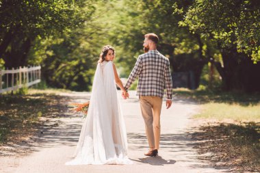 Mutlu gelin ve damat el ele tutuşup bahçede yürüyorlar. Park Ormanı 'nda yürürken el ele tutuşan çekici, yeni evlilerin arka planı. Gelecekteki yaşama giden yol. Mutlu evlilik anları