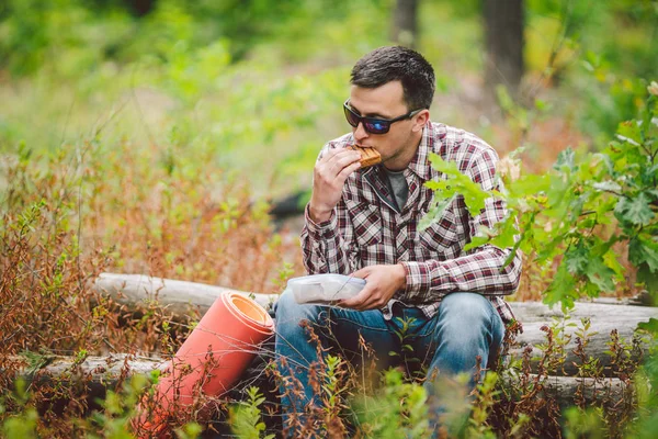 Hungry man eating. Sandwich outdoors. hiker eating sandwich sitting in forest. tourist eat snack food. Hiker take break with time for food. Caucasian guy tourist bring splastic box with sandwich