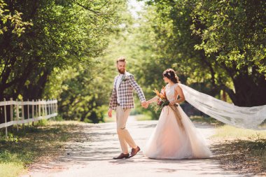 Güzel bir düğün çifti ormanı. Gelin ve damat, beni takip edin, evli çift, beyaz gelinlik ve duvak giyen kadın. Kırsal kesim aşk hikayesi. Hipster fotoğrafımı takip et. Yeni evliler el ele yürüyorlar.