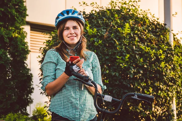 Cep telefonu tutan neşeli bir kızın portresi. Açık havada bisiklet paylaşım uygulaması kullanan mutlu gülümseyen bir öğrenci. Sokaklarda akıllı telefon uygulaması kullanan, bisikletli şık hippi kız. — Stok fotoğraf