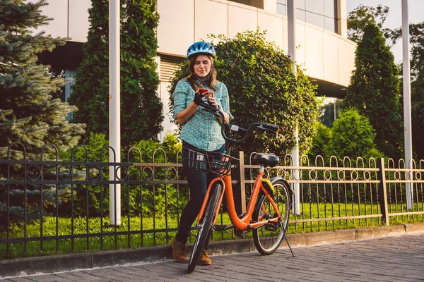 Cep telefonu tutan neşeli bir kızın portresi. Açık havada bisiklet paylaşım uygulaması kullanan mutlu gülümseyen bir öğrenci. Sokaklarda akıllı telefon uygulaması kullanan, bisikletli şık hippi kız. — Stok fotoğraf