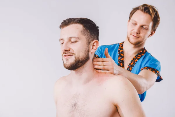 Тема масаж і тілом догляд. Красивий кавказьких чоловіків, робоче місце лікаря в блакитному рівномірної і бородою діагностування м'язи шиї та плечей, розтягування хлопець з непогана цифра масаж настільні білим тлом — стокове фото