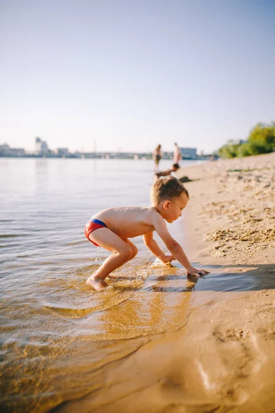 Tema es la hora de verano y el descanso cerca del agua. Poco alegre caucásico divertido chico juega y disfruta en el río. El niño está descansando y nadando en la playa de arena lago estanque —  Fotos de Stock