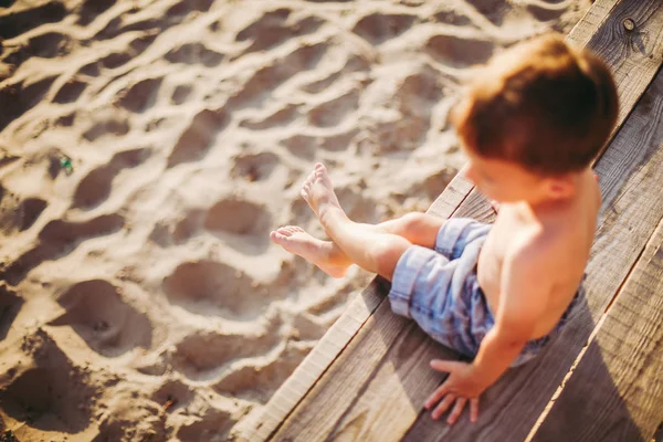 Petit garçon caucasien assis sur une jetée en bois plage de sable, heure d'été, vacances en mer près de l'eau. Le thème est le flux du temps, une vie courte, le sens et le but de l'existence. Signification de la vie — Photo