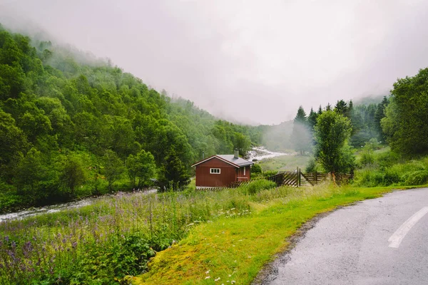 Tradycyjny norweski czerwony drewniany dom na tle lasu i przyrody z górską rzeką w deszczową pogodę z mgłą — Zdjęcie stockowe