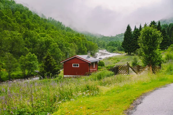 숲 과 자연의 배경에 있는 노르웨이의 전통적 인 붉은 목조 주택, 비가 오는 날씨에 안개가 자욱 한 산에 있는 강 — 스톡 사진
