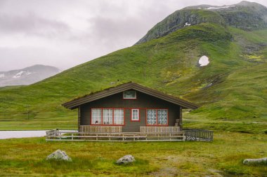 Dağdaki ahşap kulübeler Norveç 'i geçiyor. Tipik İskandinav çim çatı evleri olan Norveç manzarası. Dağ köyü, küçük evleri ve vadide çimleri olan ahşap kulübeleri var.