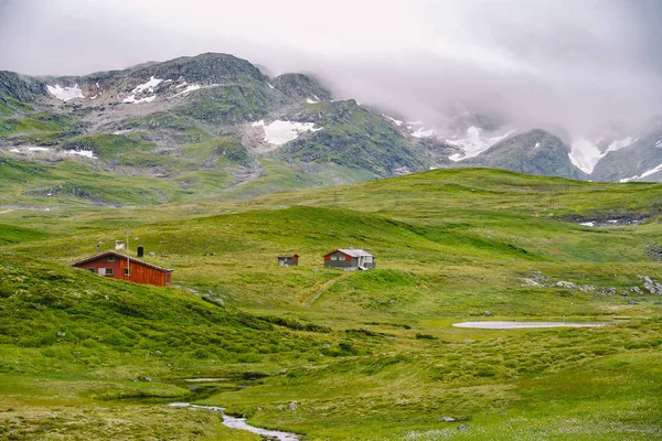 Colibă colibe de munte din lemn în trecere de munte Norvegia. Peisaj norvegian cu case tipice de acoperiș din iarbă scandinavă. Sat montan cu case mici și cabine din lemn cu iarbă pe acoperiș în vale — Fotografie, imagine de stoc