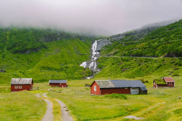 Cabaña cabañas de montaña de madera en el paso de montaña Noruega. Paisaje noruego con casas típicas de hierba escandinava. Pueblo de montaña con pequeñas casas y cabañas de madera con césped en el techo en el valle — Foto de Stock