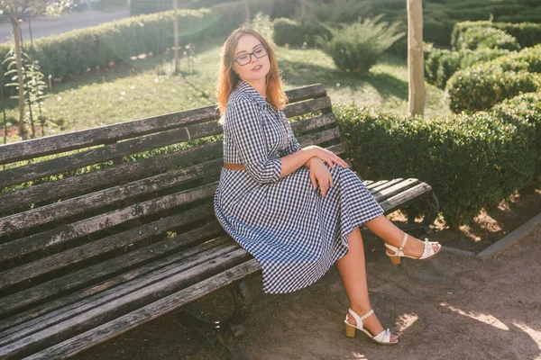 Mujer joven en la calle en vestido de verano sentado en el parque de verano en el banco. Hermosa joven en París. mujer con estilo feliz en la vieja calle de la ciudad europea. Mala visión y miopía — Foto de Stock