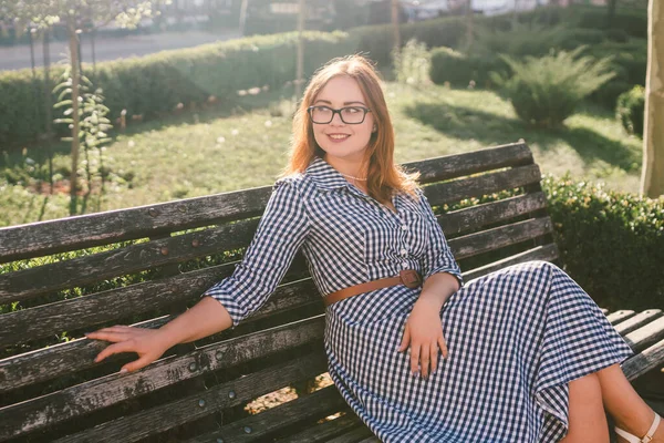 Young woman on the street in summer dress sitting in summer park on bench. Beautiful young woman in Paris. happy stylish woman at old european city street. Poor vision and myopia — Stock Photo, Image