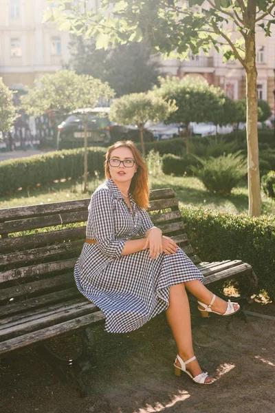 Young woman on the street in summer dress sitting in summer park on bench. Beautiful young woman in Paris. happy stylish woman at old european city street. Poor vision and myopia — Stock Photo, Image