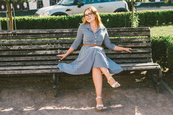 Mujer joven en la calle en vestido de verano sentado en el parque de verano en el banco. Hermosa joven en París. mujer con estilo feliz en la vieja calle de la ciudad europea. Mala visión y miopía — Foto de Stock