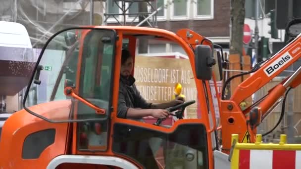 Yol işçileri yol çalışması sırasında turuncu kazıcıları çalıştırırlar. Kazı makinesi yolda. İnşaat devam ediyor. Erkek işçi kazıcı kovası kullanıyor. 15 Ekim 2018 Düsseldorf, Almanya — Stok video