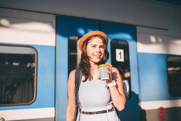 Туризм і подорожі влітку. Відпустка для студента. Працюйте і подорожуйте. Кавказька молода жінка п "є каву на платформі залізничної станції на задньому плані поїзда. — стокове фото
