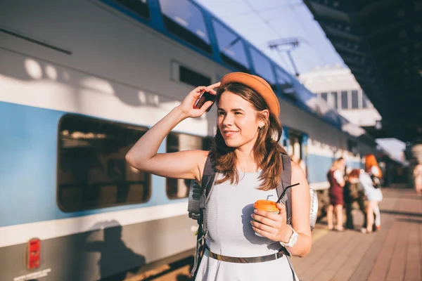 Туризм і подорожі влітку. Відпустка для студента. Працюйте і подорожуйте. Кавказька молода жінка п "є каву на платформі залізничної станції на задньому плані поїзда. — стокове фото