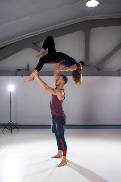 Acroyoga 和瑜伽的主题。一对两男一女站在体式的位置上。那家伙抱着那个女孩, 高高地拱起伸展的手臂。在健身房与工作室背光 — 图库照片