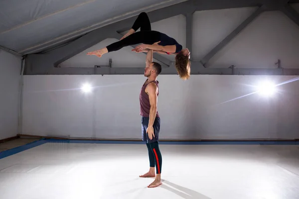 Acroyoga 和瑜伽的主题。一对两男一女站在体式的位置上。那家伙抱着那个女孩, 高高地拱起伸展的手臂。在健身房与工作室背光 — 图库照片