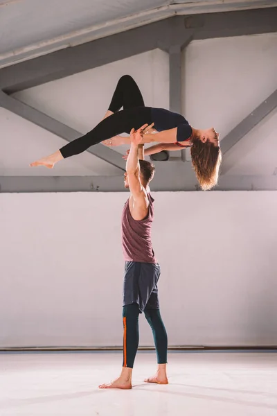 El tema de Acroyoga y Yoga Poses. Un par de dos hombres y una mujer están en la posición de asana. El tipo sostiene a la chica arqueada en el brazo extendido. En el gimnasio con un estudio de contraluz — Foto de Stock