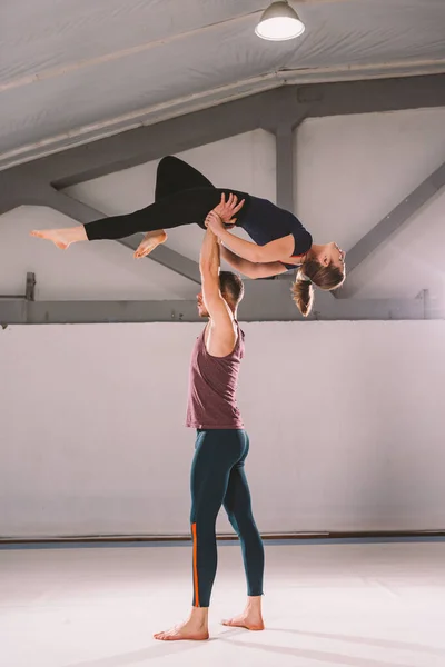 El tema de Acroyoga y Yoga Poses. Un par de dos hombres y una mujer están en la posición de asana. El tipo sostiene a la chica arqueada en el brazo extendido. En el gimnasio con un estudio de contraluz — Foto de Stock