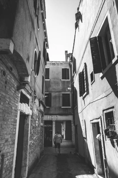 Турист с оранжевым рюкзаком и банданой прогуливается по узкой улице Европы. Италия Венеция летом. Фасад старых домов без людей и толпы туристов. Неопубликованные места в Венеции — стоковое фото
