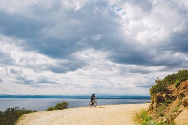 Genç adam İspanya 'da bisiklet yolunda dağ bisikleti sürüyor. Bir dağ bisikleti süren sporcu Akdeniz 'in arka planında Costa Brava' ya karşı off-road yapıyor. İspanya 'da bisiklet